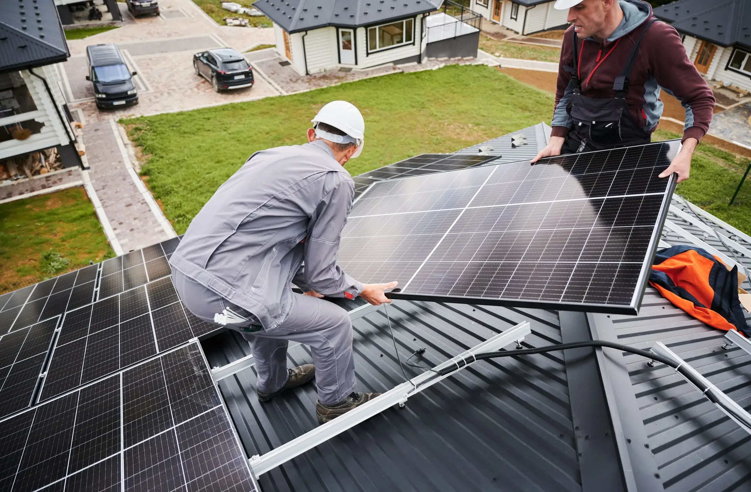 Two workers install solar panels on a residential roof